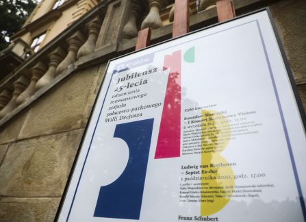 Fotografia. Plakat promujący jubileusz dwudziestopięciolecia odnowienia Willi Decjusza na tle fasady Willi.