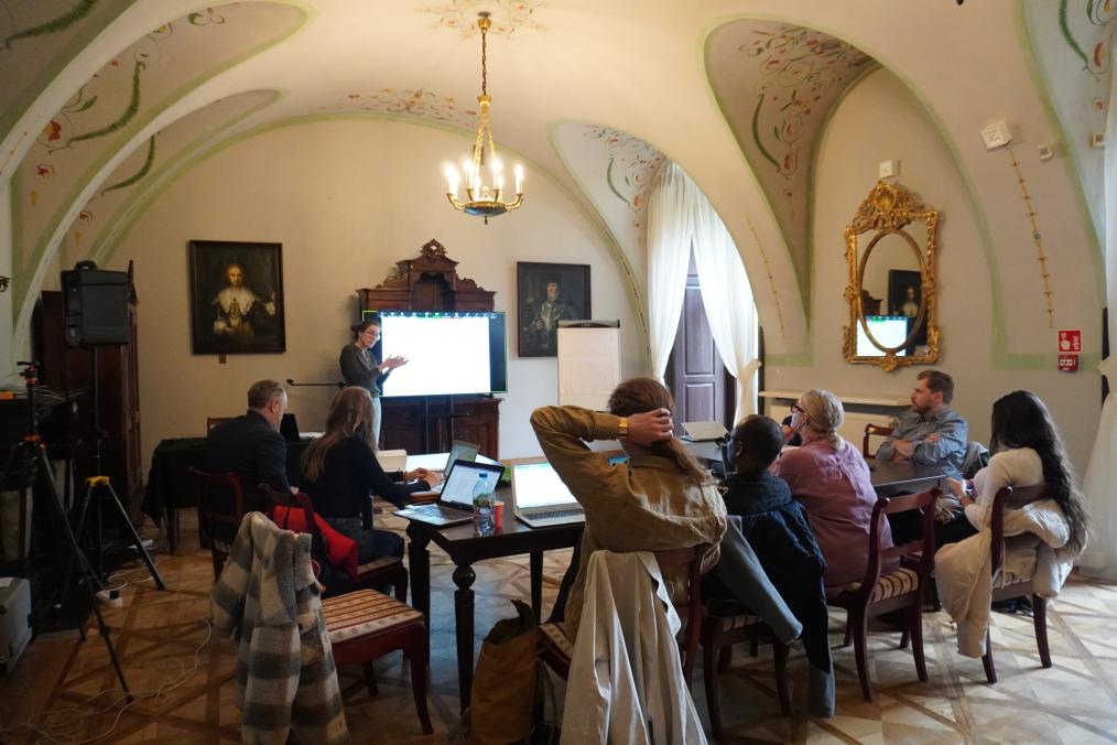 Zdjęcie grupy ludzi siedzących przy stołach i uczestniczących w prezentacji szkoleniowej