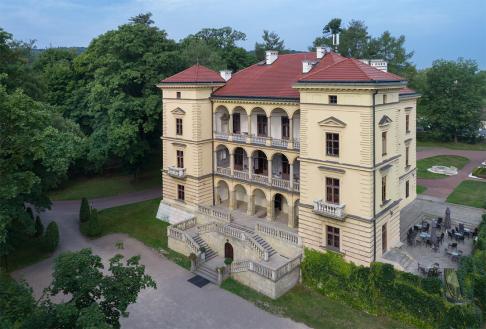 Zdjęcie fasady Willi Decjusza z dalszej perspektywy wśród drzew