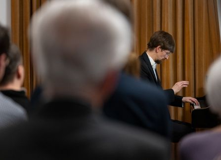 Fotografia mężczyzny z profilu w garniturze, grającego na fortepianie