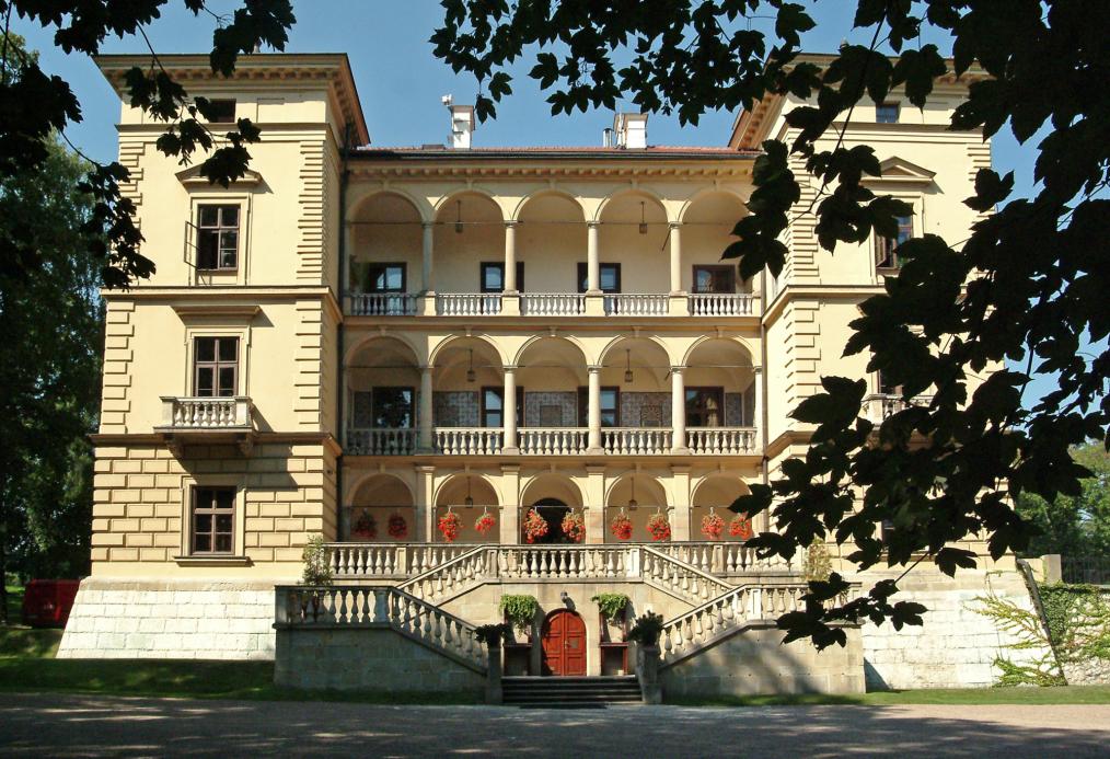 Zdjęcie fasady Willi Decjusza z dalszej perspektywy wśród drzew