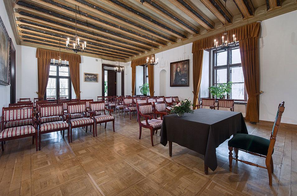 Fotografia wnętrza zabytkowej sali z rzędami krzeseł i stołem