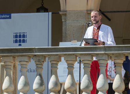 Fotografia. Mężczyzna w ludowym stroju ukraińskim przemawia ze szczytu schodów przed Willą Decjusza.