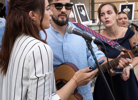 Fotografia. Trzy młode osoby występują na schodach przed Willą Decjusza, grają na gitarze i śpiewają.