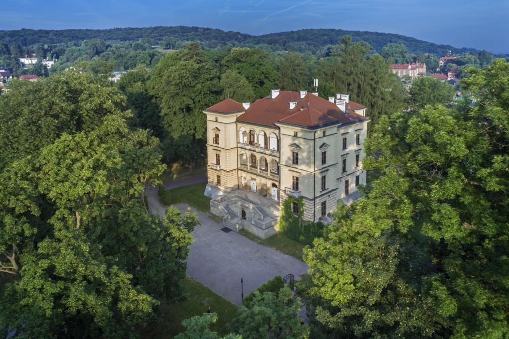 Zdjęcie budynku Willi Decjusza z dalszej perspektywy wśród drzew