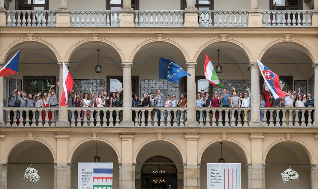 Fotografia grupy ludzi na loggii Willi Decjusza z różnorodnymi flagami