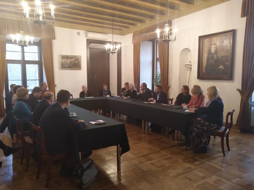 Fotografia grupy ludzi rozmawiających przy stole w zabytkowej sali