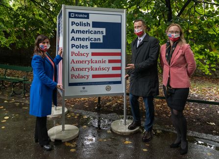 A photograph. An opening of the outdoor exhibition titled Polish Americans, American poles at planty in Krakow.  Three persons pose next to the poster promoting the exhibition.