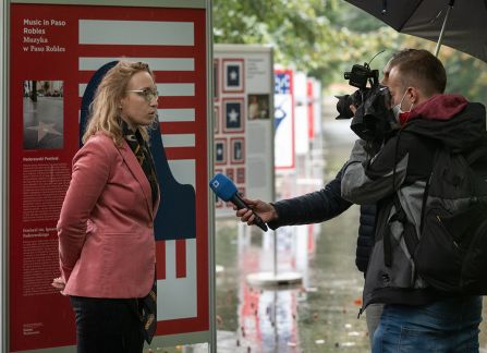 A photograph. An opening of the outdoor exhibition titled Polish Americans, American poles at planty in Krakow. the director of the Villa Decius institute for culture gives in interview in front of the camera.