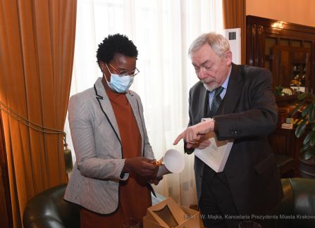 Fotografia. Wykończony ciemnym drewnem gabinet. Rezydentka ICORN Aaiun Nin otrzymuje prezent powitalny od prezydenta jacka majchrowskiego, ozdobny zestaw ceramiki. Trzyma w ręce kubek.